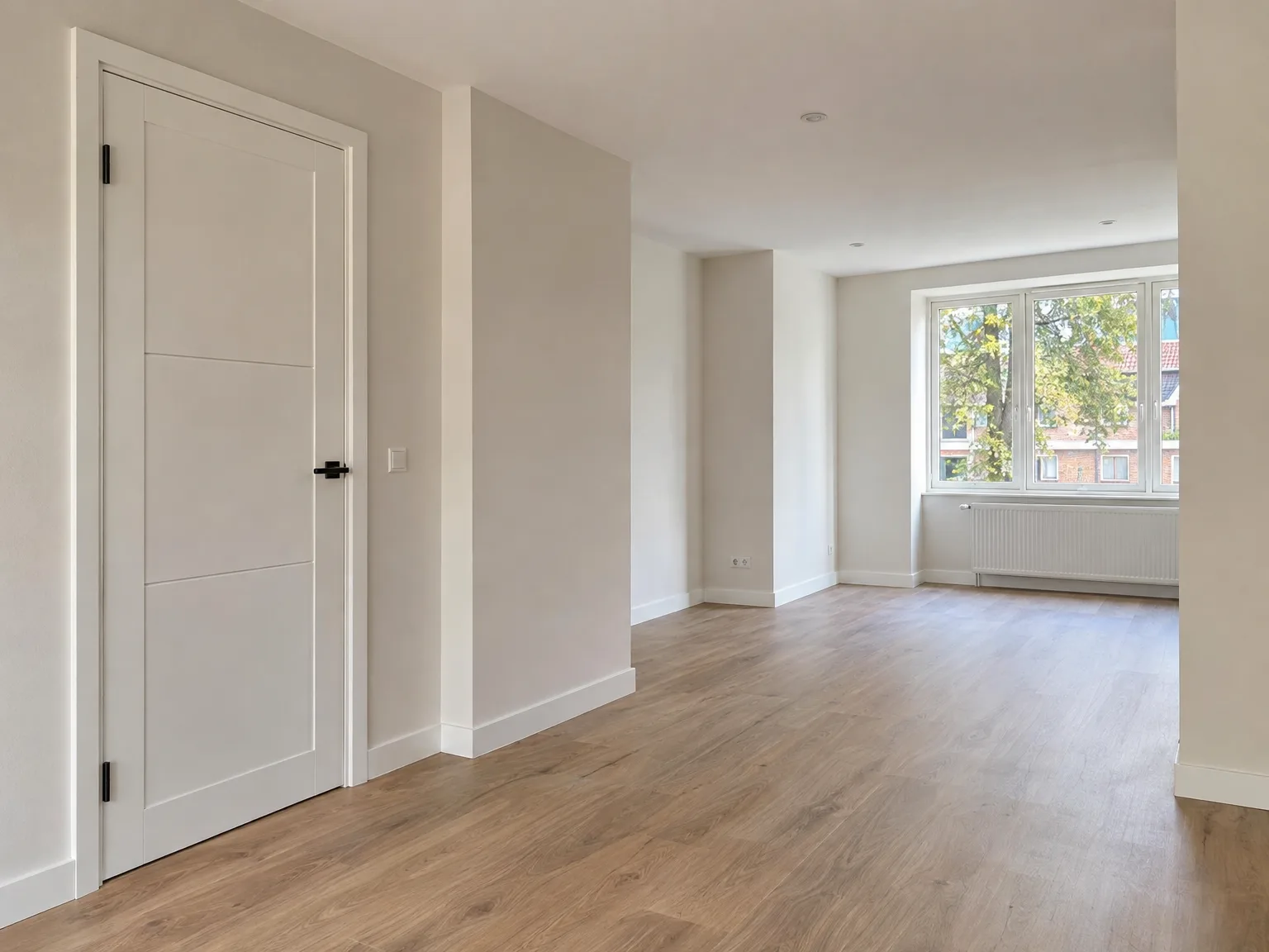 Gerenoveerde woonkamer met witte deur, houten vloer en moderne witte afwerking
