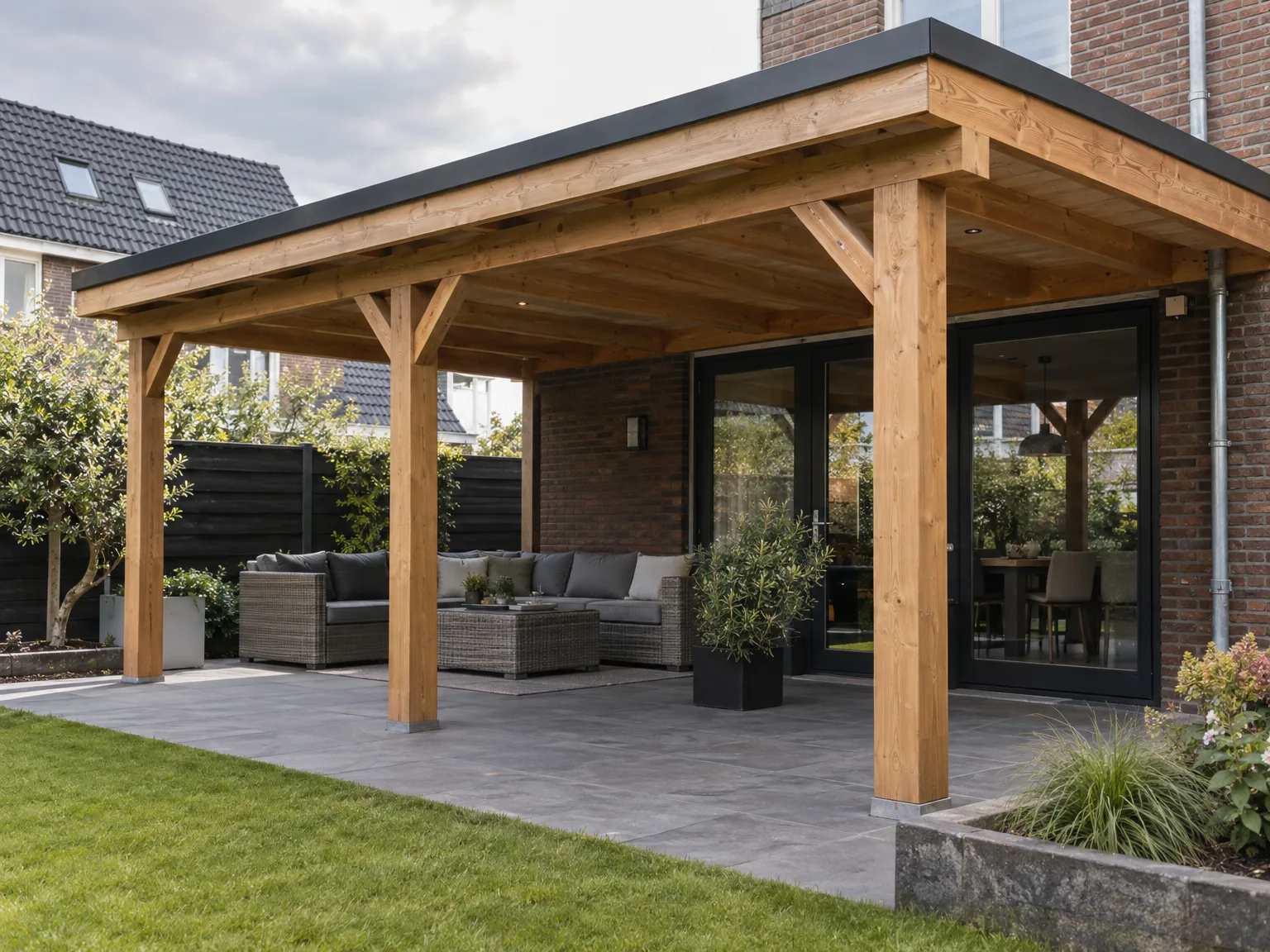 Houten overkapping boven terras met loungemeubilair naast bakstenen huis