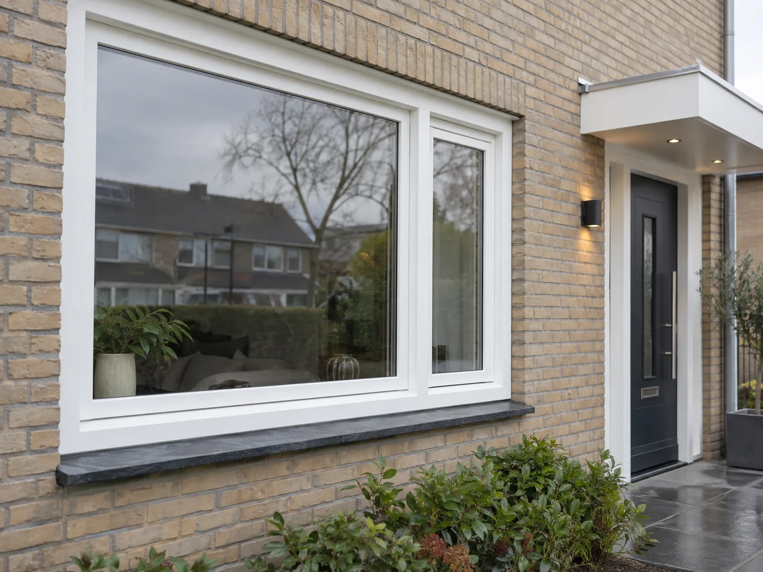 Grote witte raamkozijnen en zwarte voordeur op bakstenen gevel