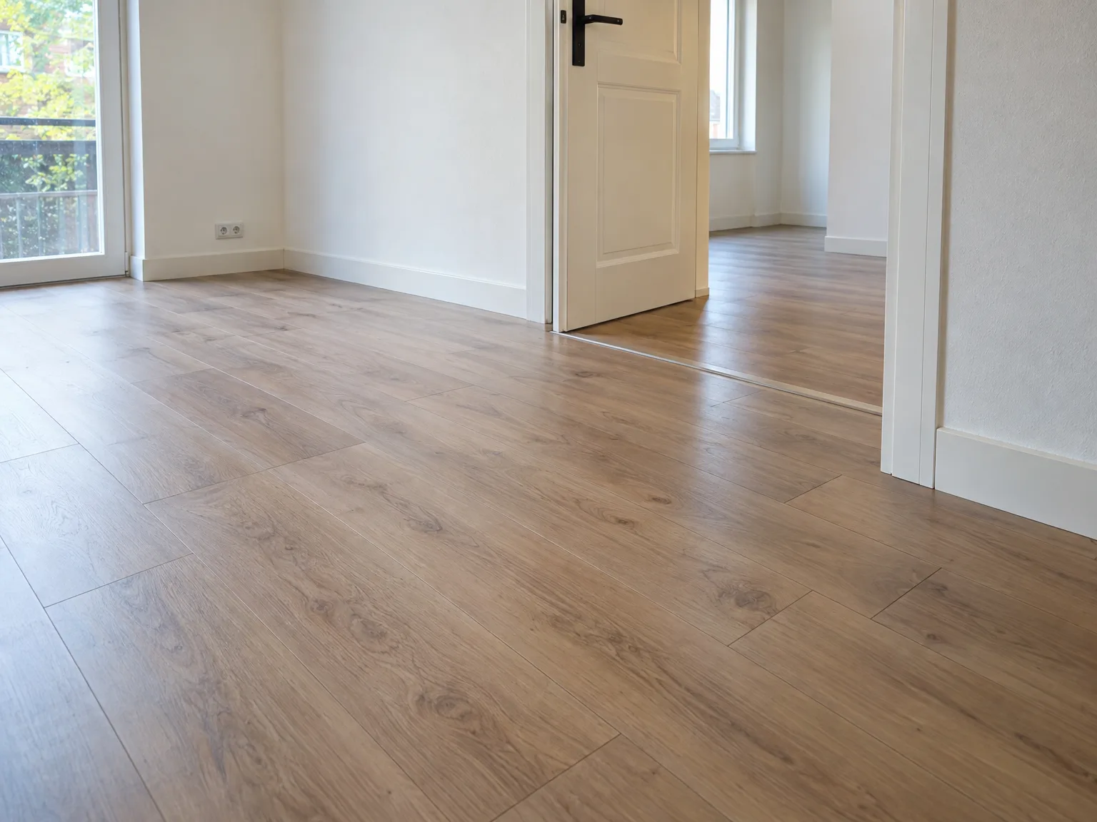 Verso gelegd laminaat in beige houtkleur in lege woonruimte met witte muren