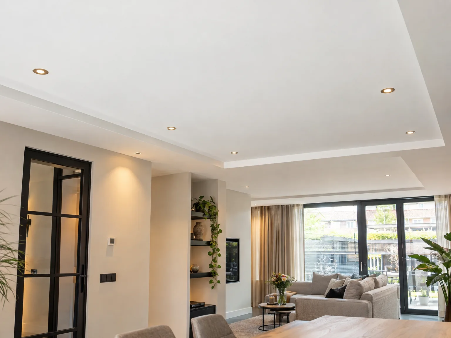 Moderne woonkamer met verlaagd plafond en LED-verlichting, inbouwkasten en zwarte glazen deuren naar terras