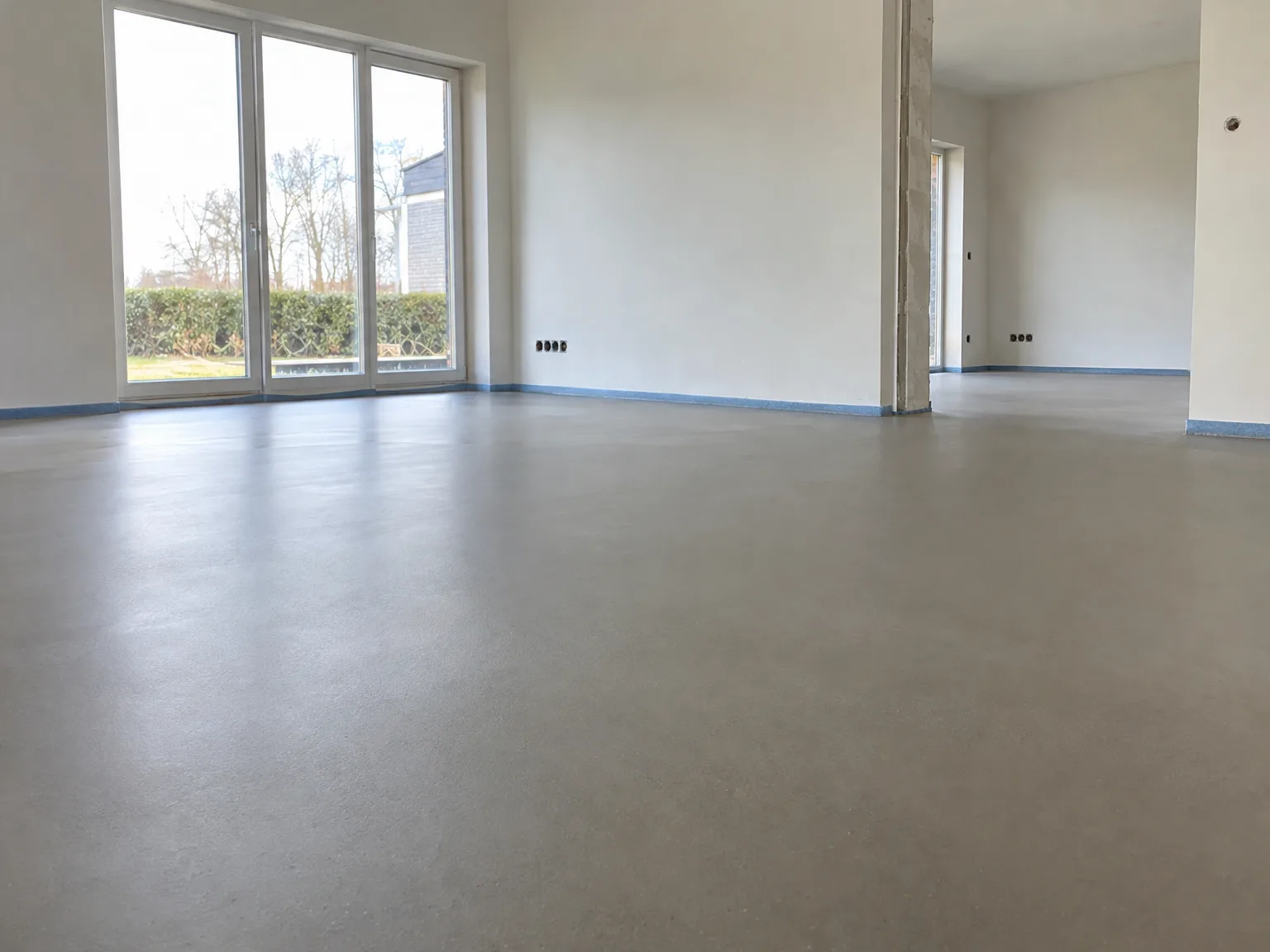 Egaliseerde vloer in moderne woonkamer met gipsplaten wanden en grote glazen deuren